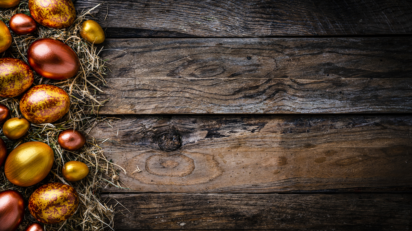 Straw nest with gold and bronze colored Easter eggs on rustic wooden table. Copy space Easter